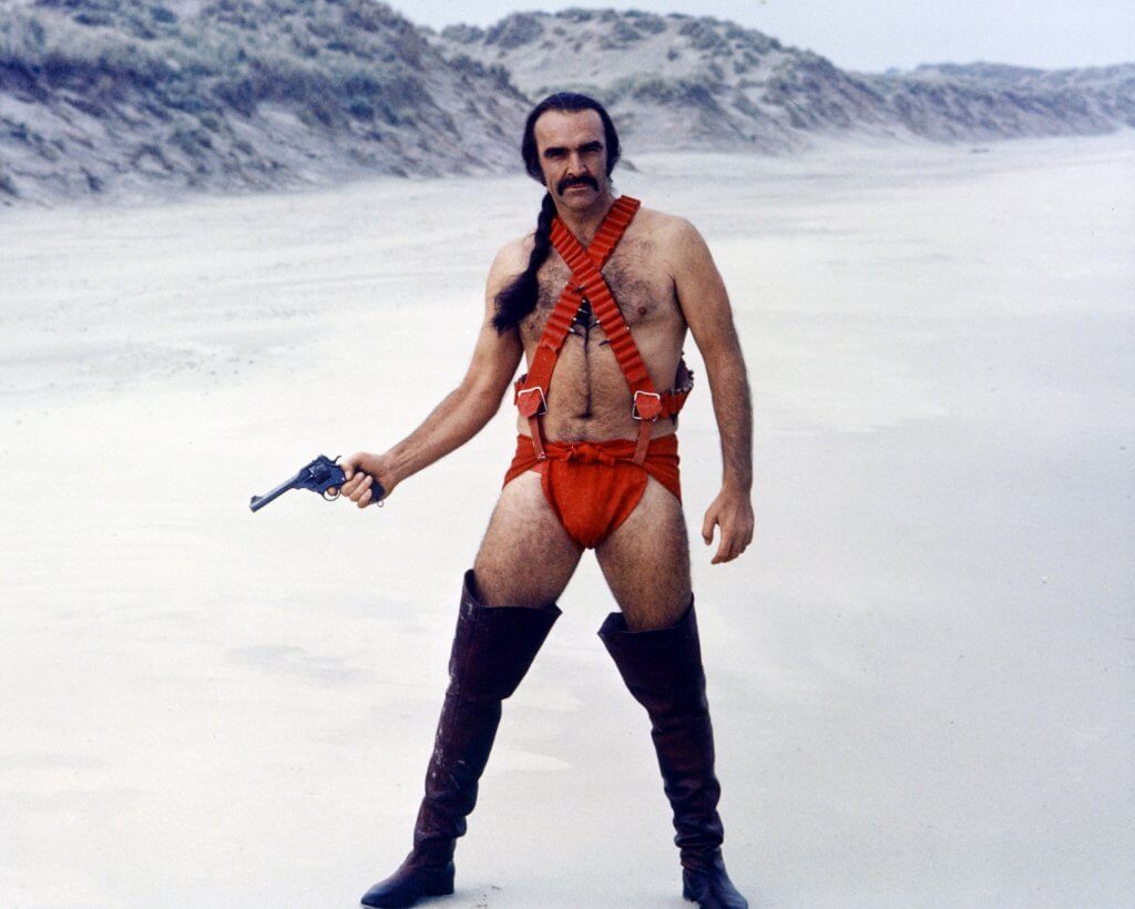 Sean Connery, British actor, holding a handgun while wearing thigh-high boots and red costume, with his hair in a pony tail, standing in a snowy landscape in a publicity portrait issued for the film, 'Zardoz', 1974. The science fiction film, directed by John Boorman, starred Connery as 'Zed'. (Photo by Silver Screen Collection/Getty Images)